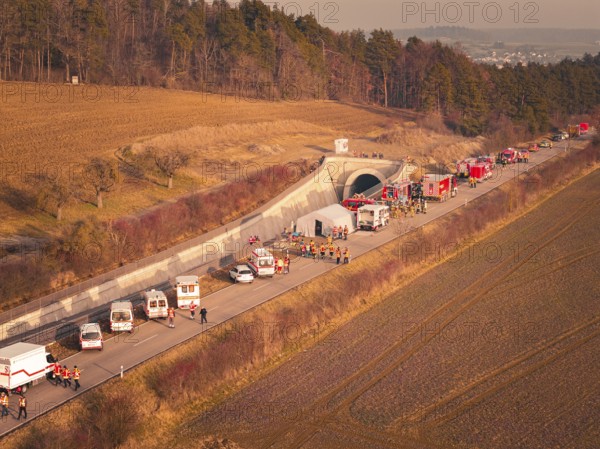 Emergency vehicles with firefighters near a tunnel next to fields and trees at dusk, fire drill on