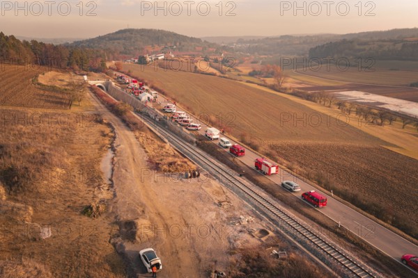Fire trucks on a country road next to railroad tracks at sunset in a hilly landscape, fire drill on