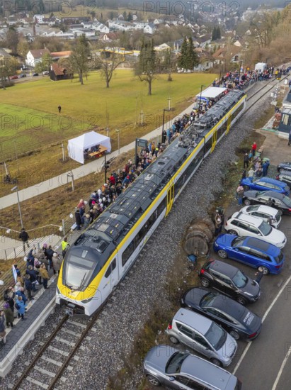A train arrives in a village, people and parked cars along the tracks, opening of the Hermann Hesse