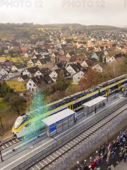 Train stops at a train station in a small town with many spectators and houses in the background,
