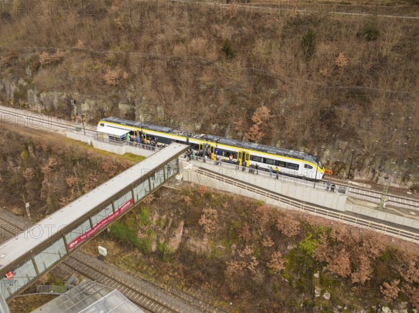 Train on tracks near a bridge with a bare hill in the background and people waiting, opening of the