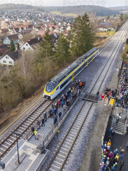 A train stops at a platform surrounded by a crowd of people. In the background you can see a
