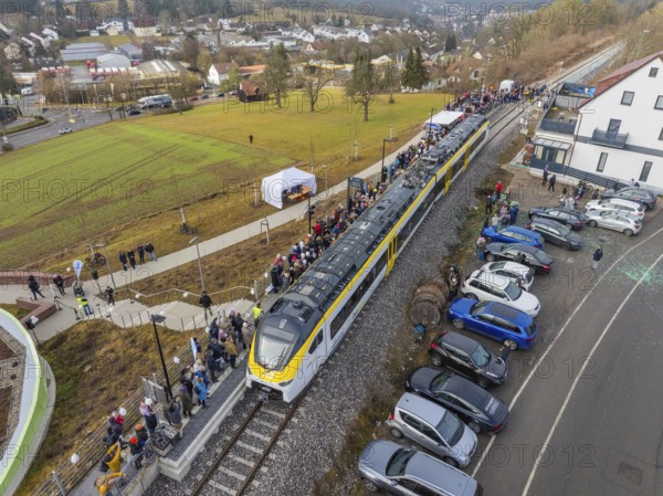 Train at a train station with people waiting and parked cars in a rural urban landscape, opening of