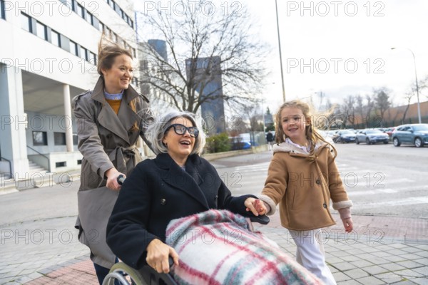 Family members, including a young girl and her mother, are pushing an elderly grandmother in a