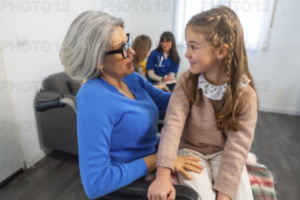 Grandma in a wheelchair interacting happily with her granddaughter, sharing a warm moment during a