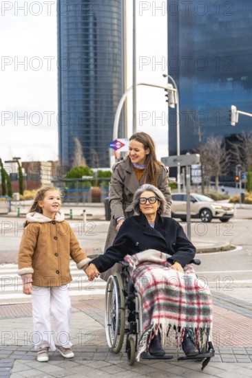 Three generations family, including little girl holding hands with her grandmother in a wheelchair,