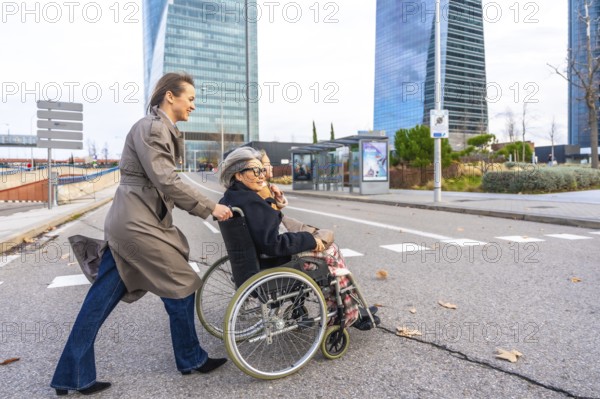 Daughter pushing a happy elderly woman in a wheelchair, moving along a modern city street with