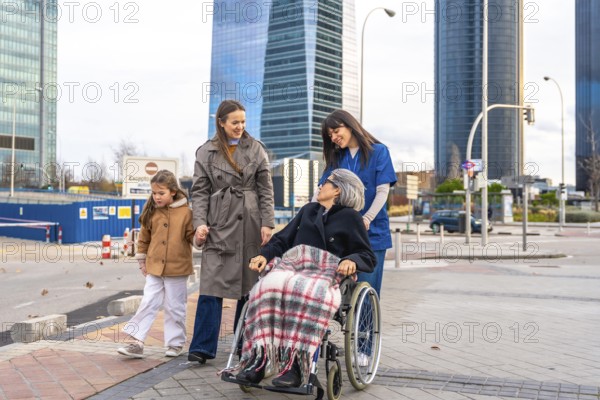 Family members and a professional caregiver are walking outdoors with a smiling senior woman in a