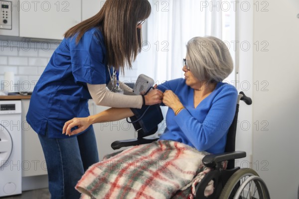 Healthcare professional in blue scrubs measuring an elderly woman's blood pressure in a wheelchair