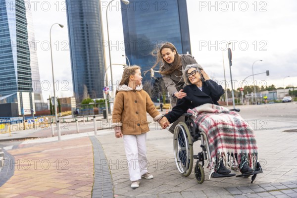 Multi generational women sharing a city walk, grandmother in wheelchair holding granddaughter's