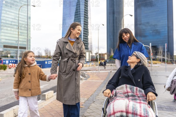 Caring caregiver pushing a senior woman in a wheelchair outdoors, joined by her daughter and