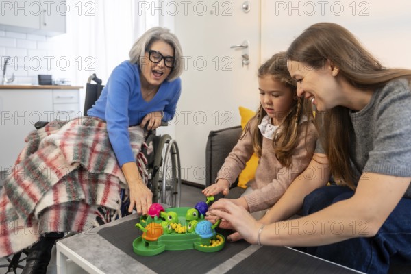 Senior woman in a wheelchair. Her daughter. And granddaughter happily playing a hungry hungry