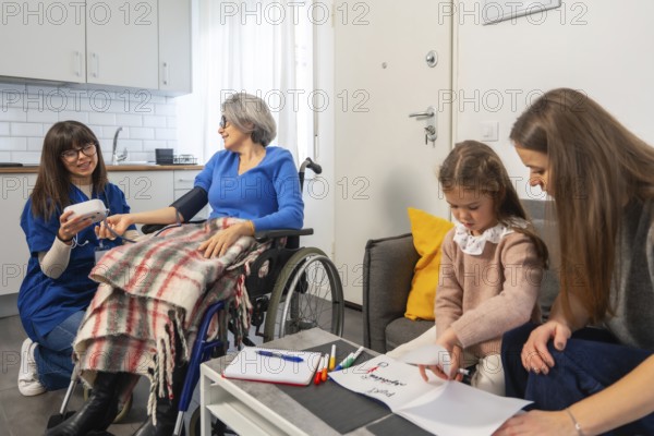 Nurse checks senior woman's blood pressure in wheelchair at home while daughter and grandchild
