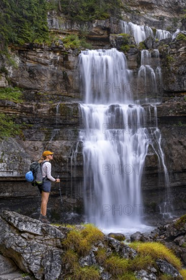 Young pretty hiker standing on rocks in front of Cascata di Mezzo waterfall, long exposure,