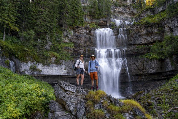 Two hikers standing on rocks in front of Cascata di Mezzo waterfall, long exposure, Vallesinella,