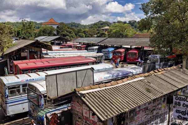 View of a bus depot with numerous parked buses and green hills in the background, Kandy bus station