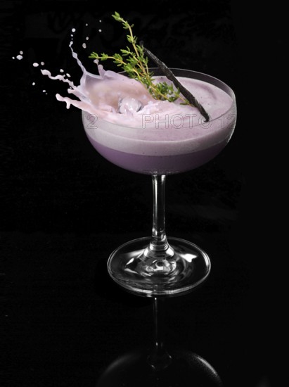 An ice cube cube falls into a cocktail cup and allows the liquid to splash on, studio shot against
