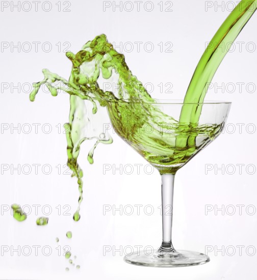 A powerful flood of green liquid pours into a cocktail glass and spills over, studio shot against a
