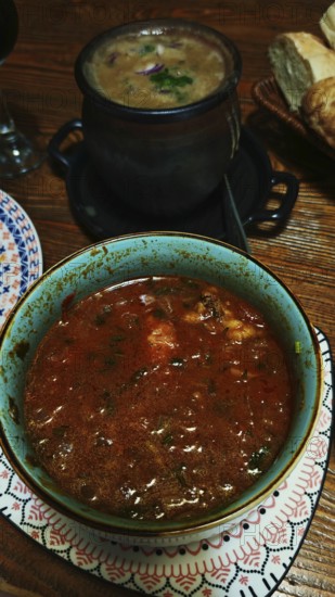 Green bowl with a delicious, rich red Georgian soup, Kharcho and a black pot in the background on a