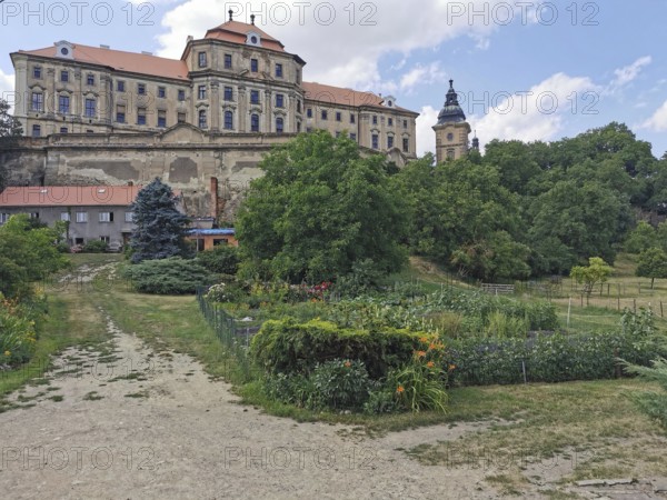 View of a monastery, castle with garden in the foreground, surrounded by lush vegetation on a