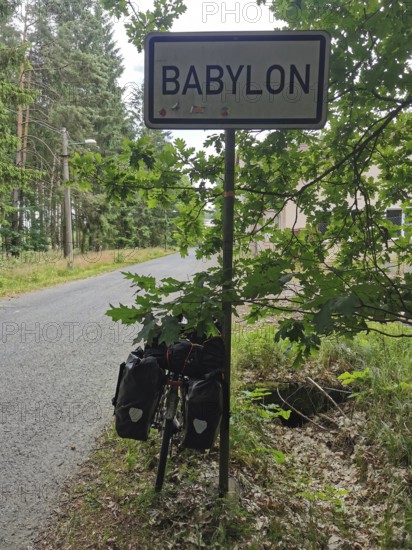 Bicycle with luggage bags in front of a Babylon town sign on a road through the forest, Czech