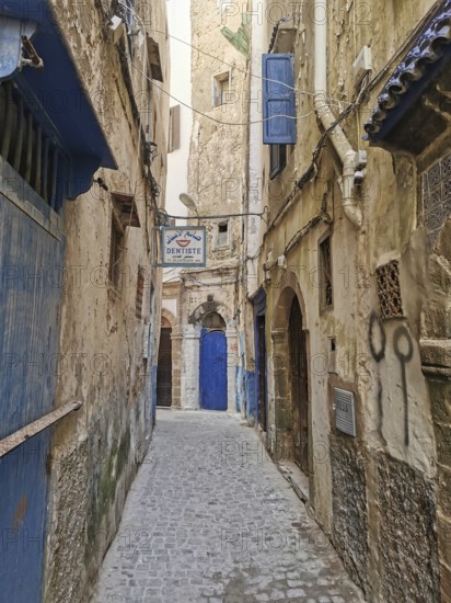 Narrow old town alleyway with weathered doors and the sign of a dentist, dentist, under a blue sky,