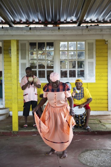 Guatemalan woman in traditional dress singing and dancing, men playing music in the back, Garifuna