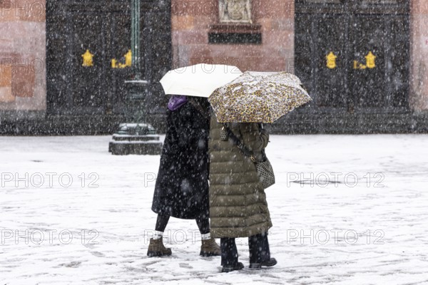 Two passers-by walk across Frankfurt's Römerberg with umbrellas. Heavy snowfalls have caused