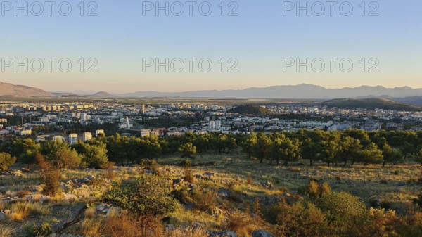 A city surrounded by nature with trees in the foreground and mountains in the background,