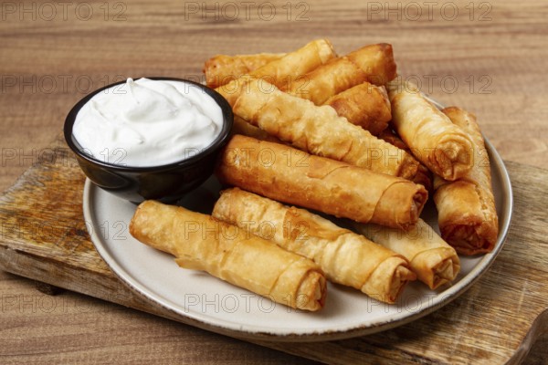 Fried spring rolls with cheese, on a wooden background, with cream sauce, no people