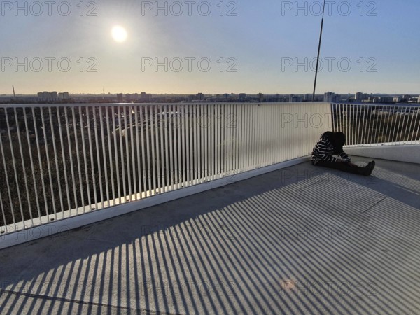 A person sitting alone on a railing with a view of an urban landscape at sunset, abstract, stripes,