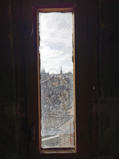 View through a narrow window of a city with church towers and a Ferris wheel under a cloudy sky