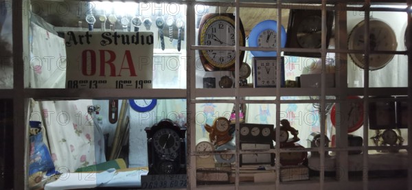A shop window of an art workshop with various clocks and a sign, illuminated at night, Berat,
