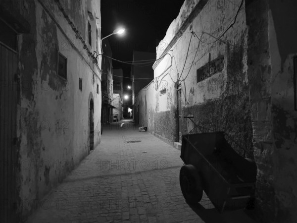 Abandoned old alley in nighttime darkness, faintly lit by black and white lanterns, Essaouira,