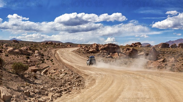 A vehicle drives on a dusty desert road through rocky landscapes under blue skies, The landscape of