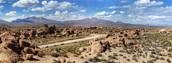 Wide panoramic landscape with large rocks, a dusty desert and mountains under a cloudy sky, The