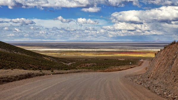 A dirt road leads through a vast, hilly landscape under a cloudy sky, The Landscape of the