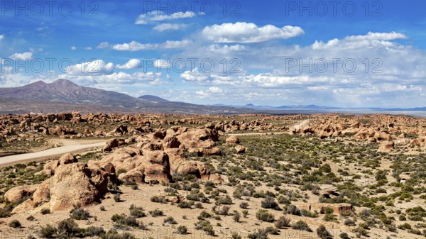 Desert landscape with a road leading through rocks and mountains, under a sky with clouds, The