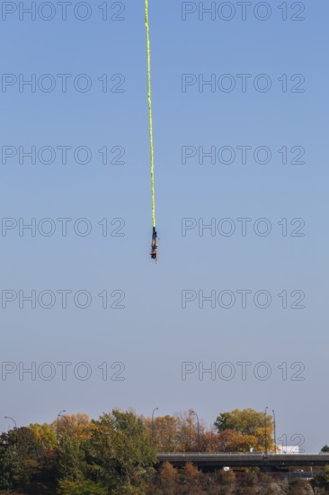 Female bungee jumper in midair with her ankles tied to a long yellow elastic bungee jumping cord,