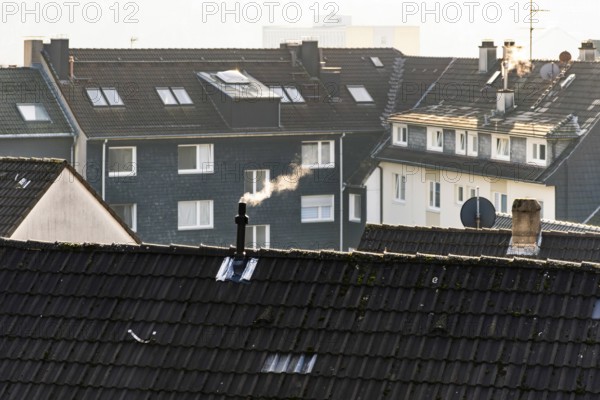 Smoke plume from a chimney over densely built residential area in the evening light, wintry city