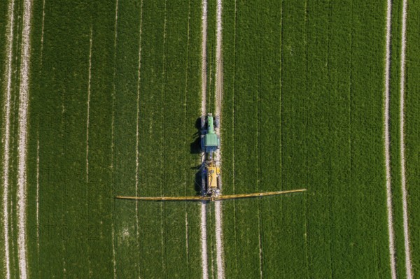 Aerial view over agricultural trailed field sprayer pulled by tractor spraying crop on farmland,