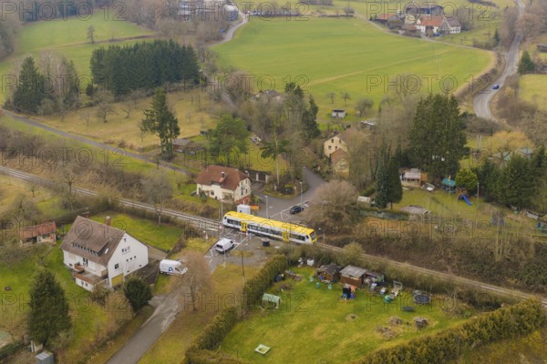 Rural scene with yellow train on rails, surrounded by trees and houses in the countryside,