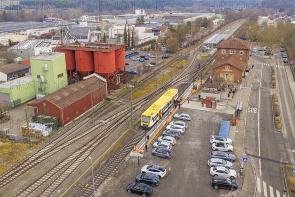Railway station with yellow train in a rural area, surrounded by cars and buildings, acceptance of
