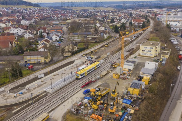 Construction site in urban area with yellow train and crane, surrounded by residential buildings,