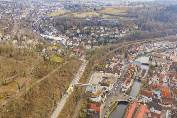 Panoramic picture of a city with river and railroad tracks, surrounded by wooded hills, acceptance
