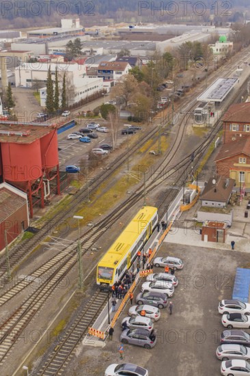 Yellow train at a train station surrounded by vehicles and buildings from a bird's eye view, taking