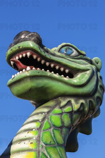 Green dragon with big teeth and long red tongue against blue sky background, Fun Show traveling