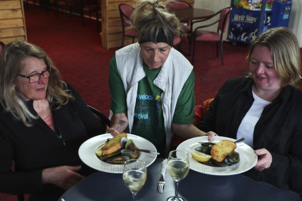 Two woman are served plates of mussels at a restaurant table by a waitress, Havelock Hotel,