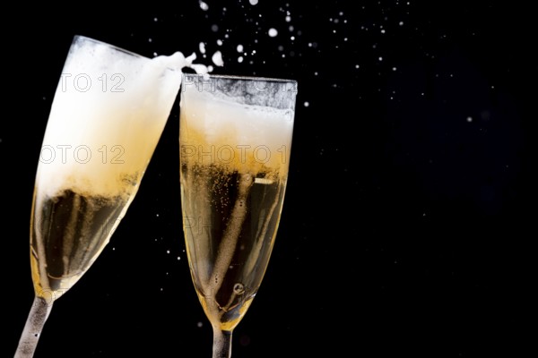 Two glasses of champagne touching each other with splashes against a dark background