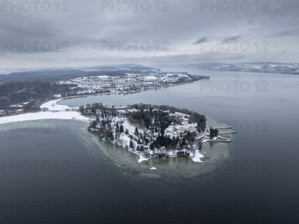 The wintry and snowy Mainau island in Lake Constance with the pier and the baroque Mainau Castle,